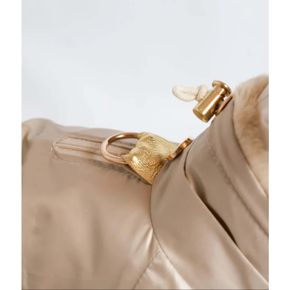 Gold-tone metal zipper pull with textured leather finish and white fabric loop on beige kombinezon dla psa with fur lining