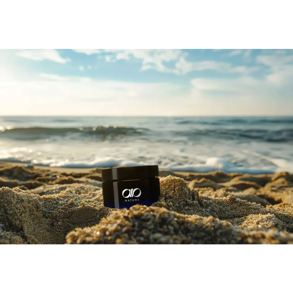 Czarny cylindryczny słoik z logo ’aio nature’, stojący na piaszczystej plaży.