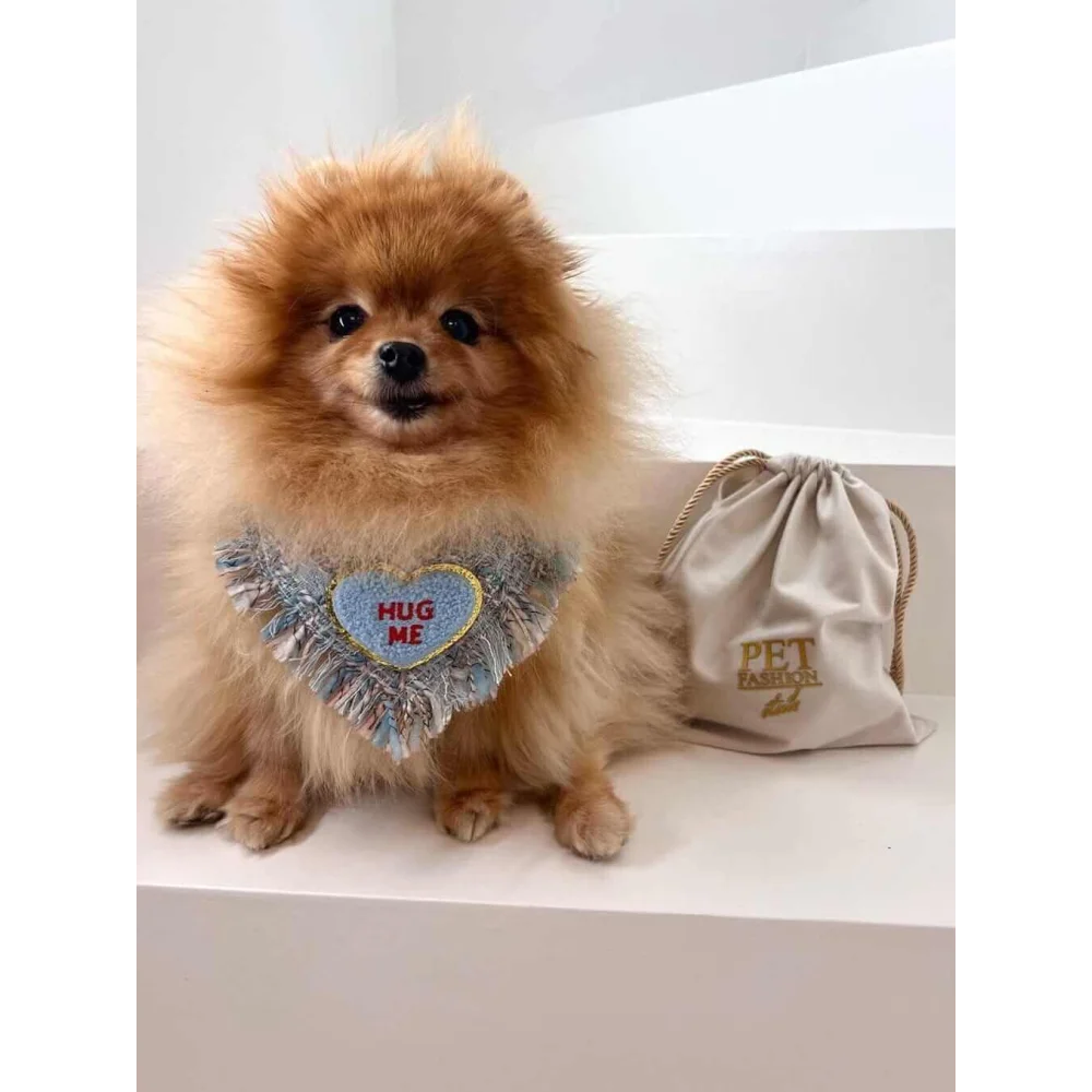 Fluffy tan pomeranian wearing a blue tweed true love coco heart-shaped fringed bib with hug me embroidery