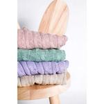 Stack of beige pastel-colored sweterek wełniany with textured cables neatly folded on a stool that chroni szyję pupila