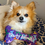 Fioletowa zabawka w kształcie kości z kolorowymi kreskówkowymi wzorami i tekstem ’pawty animal!’ wyszytym na biało.