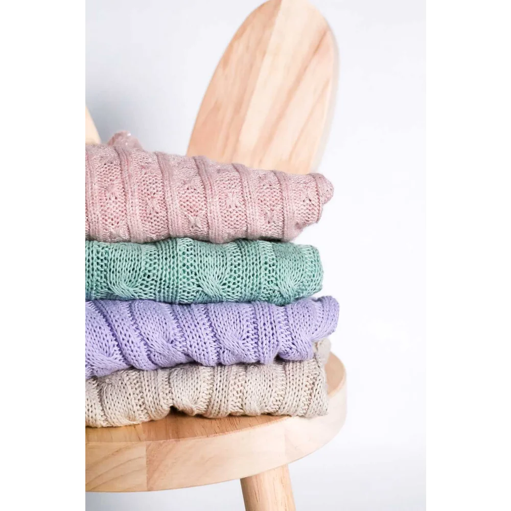 Stack of pastel-colored knitted wool sweaters with cable patterns on a wooden stool for pet fashion etoile chroni szyję pupila