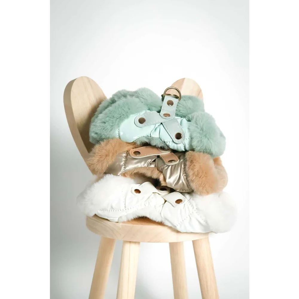 Stacked on a wooden stool are szelki bezuciskowe dog harnesses with miękka futrzana podszewka in mint green gold and white