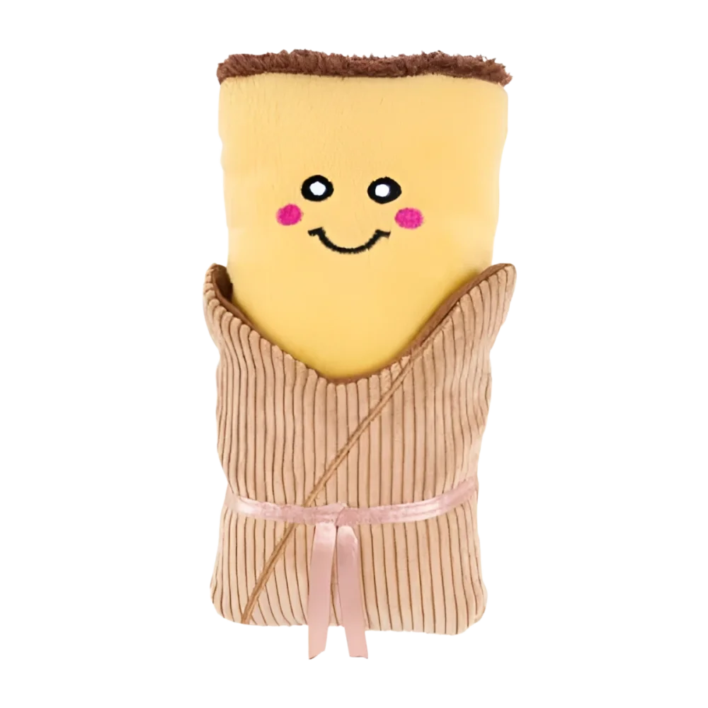 Pluszkowa, żółta ręcznik w kształcie burrito z uśmiechniętą twarzą i różowymi policzkami, owinięta w beżowy materiał z prążkowanej tkaniny, przewiązana pasującą wstążką.
